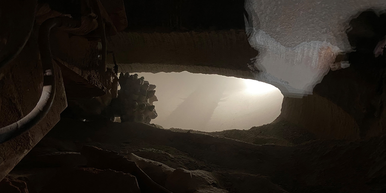 A roadheader is shown in the foreground after holing through the tunnel and seeing light on the other side.