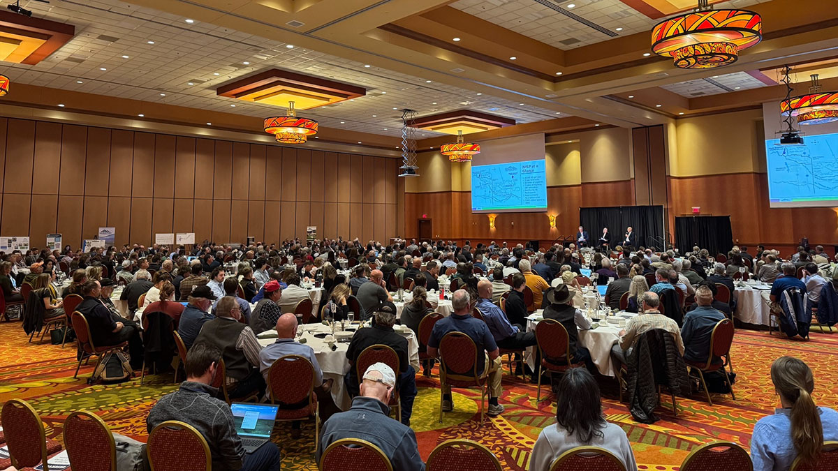 People sit at tables in conference room listening to a speaker standing on a stage
