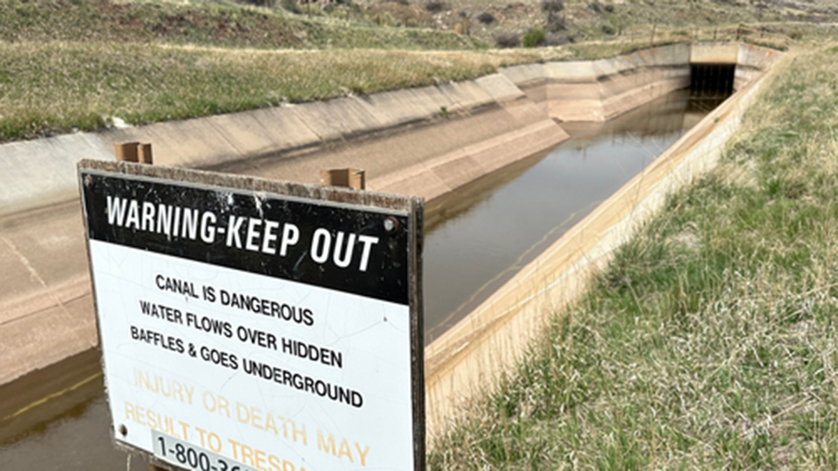A sign in front of a canal says "warning, keep out." In back on the left side of the canal is a ramp that game animals can use to escape.